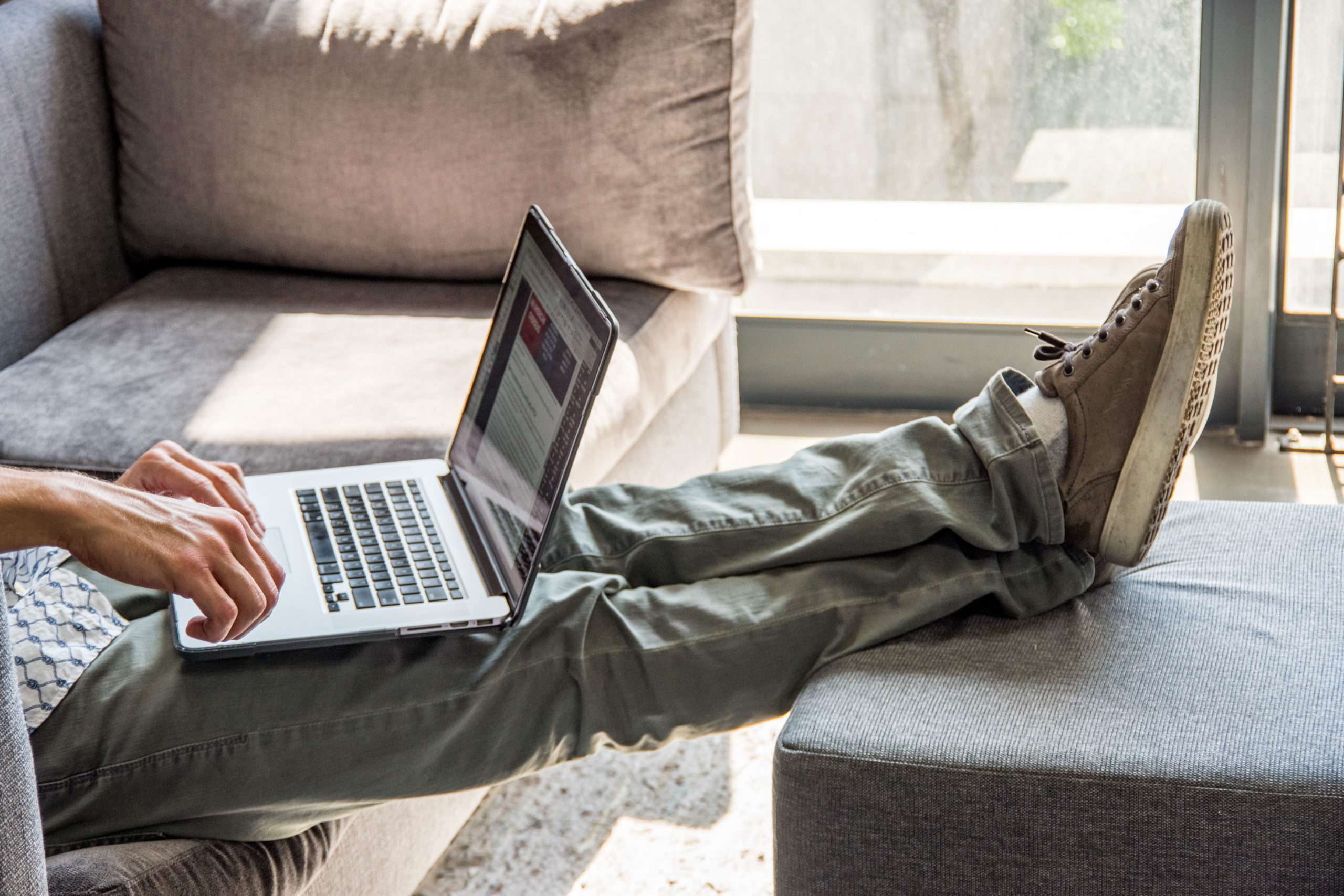 man on couch with laptop resting feet on an ottoman